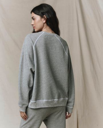 A woman stands with her back to the camera against a neutral backdrop, wearing THE GREAT. CORE KNITS' The Slouch Sweatshirt in Varsity Grey with fuller sleeves, paired with matching pants.
