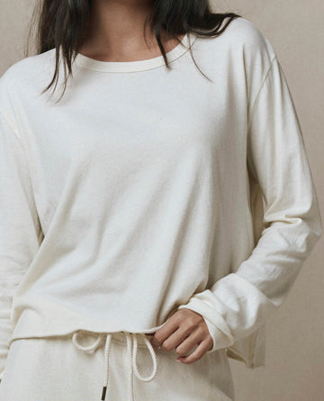 A person wears THE GREAT. CORE KNITS The Long Sleeve Crop Tee in Washed White, a loose-fitting, long-sleeve top with raw hem, paired with matching drawstring pants and one hand resting at the waist.