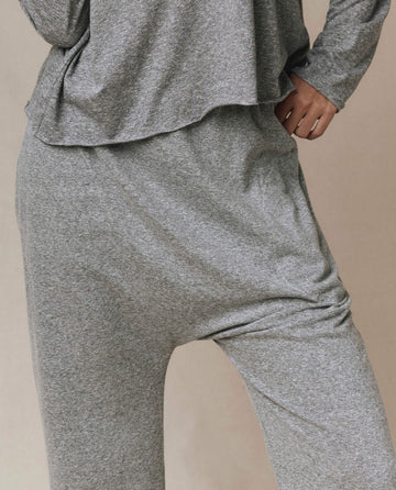 Model wears THE GREAT. CORE KNITS The Jersey Crop Pant in heather grey, featuring a loose fit, elastic waist, and straight leg; only torso, hips, and upper legs visible with left hand on hip.
