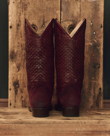 The Basket Weave Cowboy Boot in oxblood by THE GREAT. F26 STETSON stands upright on a worn wooden surface, set against a rustic wooden backdrop.