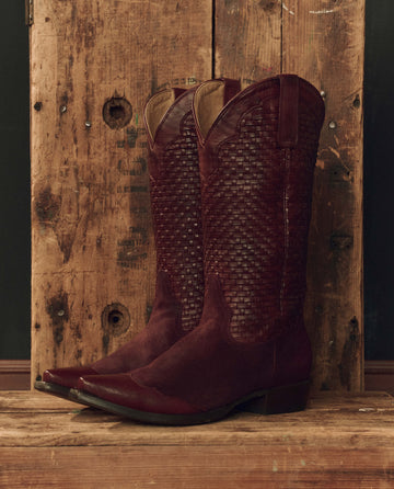 The Basket Weave Cowboy Boot in Oxblood by THE GREAT. F26 STETSON is displayed against a rustic wooden background.