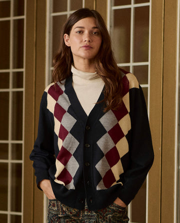 The Argyle Menswear Cardigan in navy worn over a cream turtleneck, featuring a button-front argyle pattern in maroon, cream, and grey.