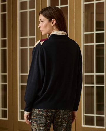 THE GREAT. H26 Argyle Menswear Cardigan in navy blue with long sleeves and a multi-colored argyle pattern across the shoulders.