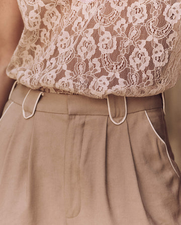 Someone wearing a white lace top and The Western Maker Trouser in Barley by THE GREAT. SP25 D1, featuring belt loops and white piping detail.