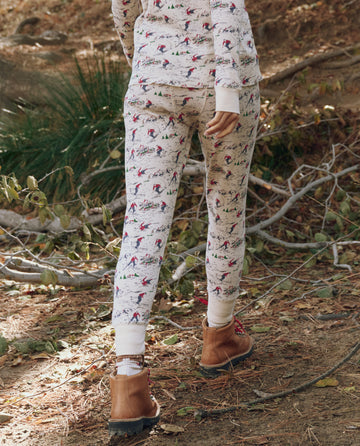 Someone wearing THE GREAT. F25 TGO’s The Union Long John in Slopeside Print steps outside, walking along a dirt path scattered with branches and leaves, paired with tan boots.