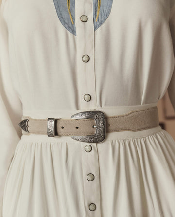 Close-up of The Western Narrow Belt – Cream With Silver by THE GREAT. STETSON SP26, shown with a cream-colored dress, metal snap buttons, and an ornate silver buckle.