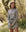 A person in a long-sleeve, floral-patterned outfit outdoors with trees and grass mirrors the unique style celebrated by fans of THE GREAT. SP25 TGO's The Quarter Zip Trail Pullover in Falling Daisy.