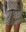 A person outdoors with hands in pockets is wearing the Falling Daisy Rover Short and a matching floral-patterned shirt from THE GREAT. SP25 TGO, epitomizing casually stylish men's clothing.