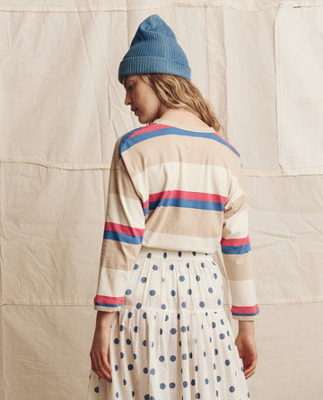A person wearing a blue knit beanie and THE GREAT. PS26 The Shrunken Henley. Novelty -- Study Hall Stripe, paired with a white skirt with blue polka dots, standing with their back turned.