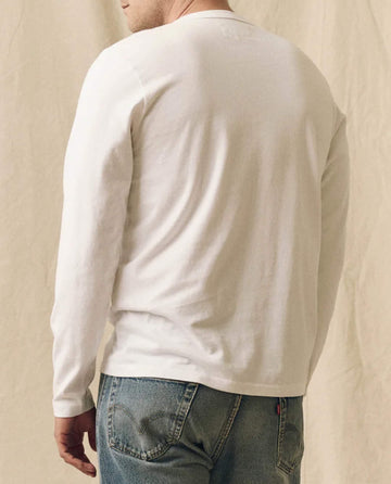 A person wearing THE GREAT. FALL 23 MEN The Men's Pure Knits Long Sleeve Slim Crew in True White and blue jeans stands with their back to the camera against a neutral background.