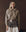 A woman stands against a dark background, wearing THE GREAT. F25 D1 The Crochet Collar Pullover in Oat with Brown, styled with a wide belt and a white skirt featuring a dark lace overlay.