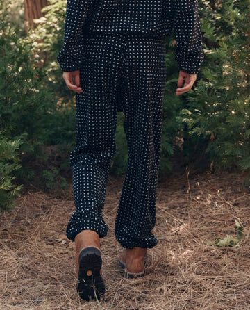 Wearing The Campfire Sweatpant. -- Black Dot by THE GREAT. F26 TGO, someone strolls on a pine-covered forest floor surrounded by green trees.