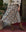 A person wearing a cream knit sweater, brown cowboy boots, and THE GREAT. PF25's The Canary Skirt in Indigo Floral stands on red tiles near potted plants, embodying a unique blend of fashion and charm.