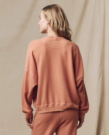 A person with blonde hair, viewed from the back, is wearing The Teammate Sweatshirt in Sun Dried Orange by THE GREAT. SU24 KNITS and matching pants, standing against a neutral backdrop. The ensemble features vintage details that add a timeless touch to the look.