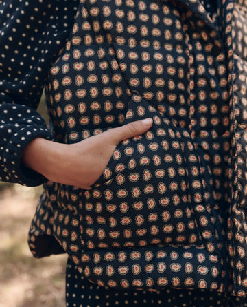 Close-up of a hand in the pocket of The Polar Vest. -- Black Paisley by THE GREAT. F26 TGO, layered over a polka dot long-sleeve shirt.
