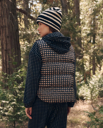 Person standing in a forest, side view, wearing THE GREAT. F26 TGO The Polar Vest. -- Black Paisley, a striped beanie, and matching patterned pants.