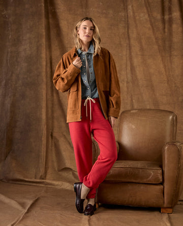 A woman wearing a brown jacket, denim shirt, and The Fleece Stadium Sweatpant -- Campfire with dark brown loafers.
