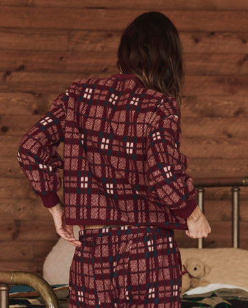 In a cozy wooden room, an individual stands with their back to the camera, showcasing the soft fleece fabric of The Plush Fleece Henley Sleep Sweatshirt in Fireside Plaid by THE GREAT. HOL 24 SLEEP.
