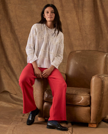 A woman wearing a white long-sleeved blouse and red The Fleece Lap Sweatpant sits on a brown leather armchair.