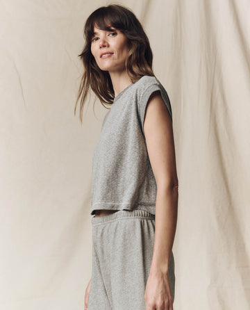 A woman in a sleeveless gray top and pants, styled with the timeless charm of "The Square Tee" from THE GREAT. SU23 CORE KNITS, stands sideways against a neutral background.