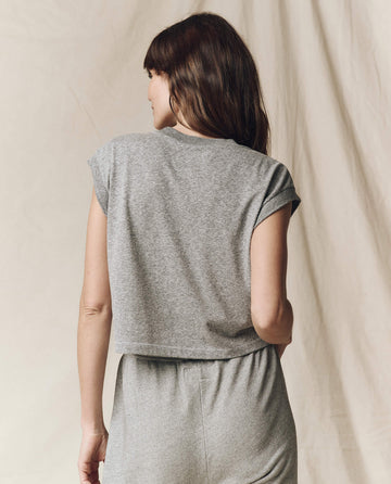 A person with long brown hair faces away, wearing The Square Tee in Heather Grey and matching pants from THE GREAT. SU23 CORE KNITS, set against a light-colored background.