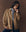 A person with long braids poses against a brown background, wearing THE GREAT. F25 D1 The Folsom Jacket -- Tobacco over a light blue shirt and dark pants.