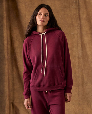 The Fleece Pullover Hoodie in plum fleece with a front kangaroo pocket and off-white drawstring cords.