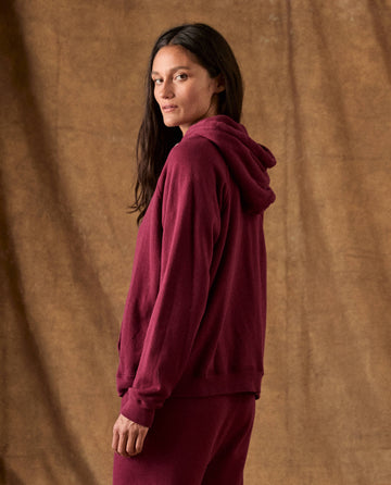 A person wearing The Fleece Pullover Hoodie in plum, looking over their shoulder.