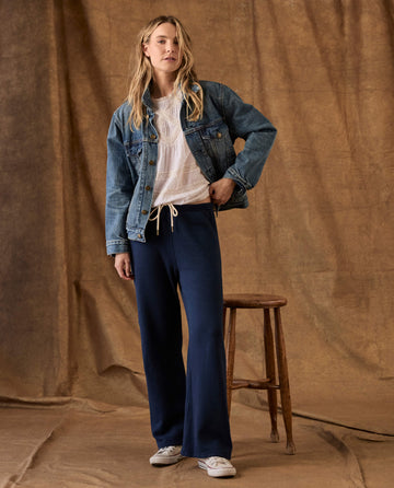 A woman wearing a denim jacket, white lace top, and True Navy The Fleece Lap Sweatpant with a drawstring waist.