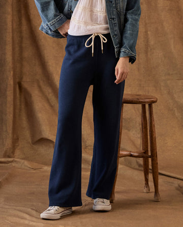 A person wearing The Fleece Lap Sweatpant in True Navy, featuring a wide-leg, drawstring fleece design.