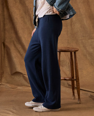 Side view of a person wearing The Fleece Lap Sweatpant in True Navy, a white top, a denim jacket, and white sneakers.