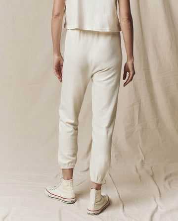 A person wearing The Stadium Sweatpants in Washed White from THE GREAT. CORE KNITS and a matching top stands on a fabric-covered floor, facing away. Their hands rest easily at their sides, while white high-top sneakers complete the look.