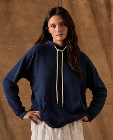 A person wears The Fleece Pullover Hoodie in True Navy, a fleece pullover with a cream-colored drawstring.