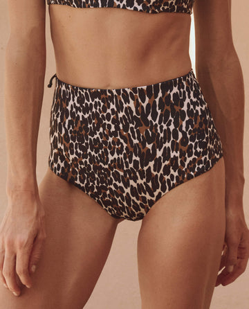 A person wears THE GREAT. SP25 SWIM The Reversible Mid Rise Brief in leopard print, paired with a matching bikini top, shown from waist to mid-thigh.