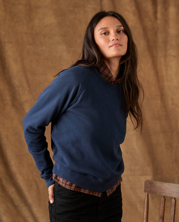 A person wearing THE FLEECE ROOKIE SWEATSHIRT -- TRUE NAVY layered over a brown plaid shirt.