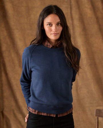 A person wearing a cozy THE FLEECE ROOKIE SWEATSHIRT -- TRUE NAVY over a brown plaid collared shirt.