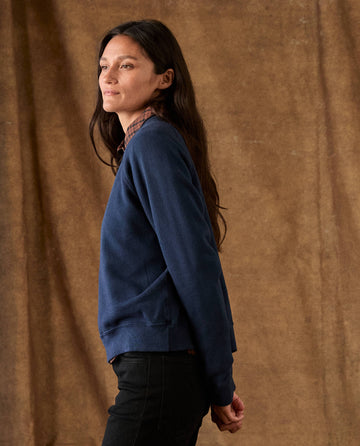 A woman wearing a cozy THE FLEECE ROOKIE SWEATSHIRT -- TRUE NAVY over a plaid shirt.