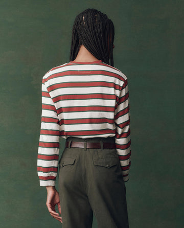 A person with braided hair faces away, wearing THE GREAT. F25 D2's The Campus Crew. Novelty in Cream Bridle Stripe and high-waisted green pants against a plain dark green background.