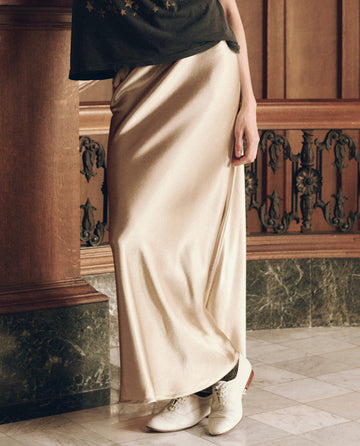 A person wearing The Elastic Bias Skirt. -- Gold Shimmer, a floor-length elastic bias skirt, paired with white lace-up shoes.