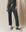 A person in "The Wide Leg Cropped Sweatpant - Washed Black" from THE GREAT. CORE KNITS and black high-top sneakers stands before a beige backdrop.