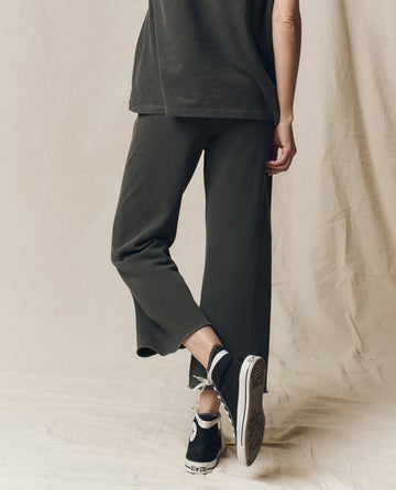 A person in wide-leg cropped sweatpants by THE GREAT. CORE KNITS with a drawstring waist, paired with black high-top sneakers, stands against a beige background.