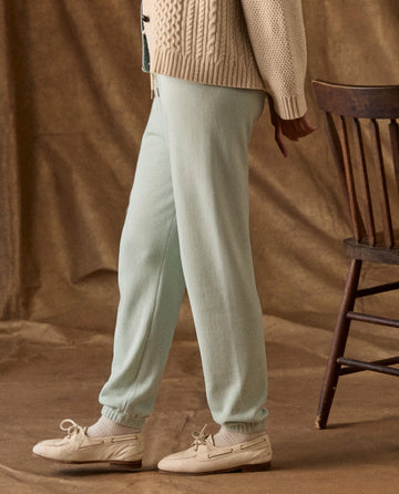 The Fleece Stadium Sweatpant in Fresh Mint, a pair of mint green French terry sweatpants with elasticized cuffs worn with beige boat shoes and a cable-knit cardigan.