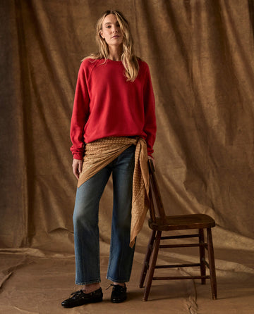 A person wears a Campfire The Fleece College Sweatshirt, blue jeans, and a tan patterned scarf tied around the waist, standing next to a wooden chair.