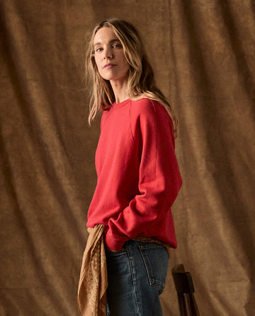 A person wears a red The Fleece College Sweatshirt - Campfire tucked into blue jeans.