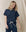 Wearing THE GREAT. FALL 23 KNITS' "The Boxy Crew" in True Navy, featuring a white drawstring, a person smiles downwards against a beige backdrop. The vintage essence of comfort shines through its 100% cotton fabric.