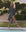 A barefoot woman in THE GREAT. SP25 SWIM The Shoreline Coverup – Leopard walks by a pool edged with trimmed hedges and stone steps.