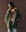 Wearing THE GREAT. F25 D1’s The Quilted Liner Parka - Army with Hot Orange, a patterned sweater, and light blue jeans, a person stands against a plain brown background, looking down with hands in jacket pockets.