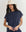 A woman wearing THE GREAT.'s The Micro Terry Wedge Sweatshirt in Vintage Blue stands against a plain background, looking at the camera.