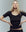 A woman with long blonde hair stands with her hands on her hips, wearing THE GREAT.'s The Baby Rib Ballet Tee in Almost Black (short sleeves) against a plain background.