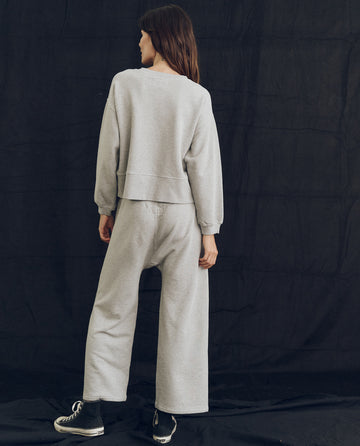 Person in The League Sweatshirt by THE GREAT. PS24 LOFTY KNITS, in Lofty Heather Grey, standing with their back facing the camera against a dark backdrop. Handcrafted locally in Los Angeles.